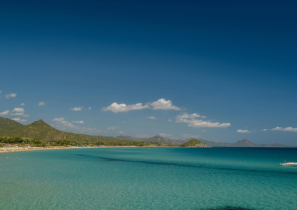 Vue panoramique sur une plage aux eaux turquoise bordée de collines verdoyantes sous un ciel bleu, paysage côtier méditerranéen.